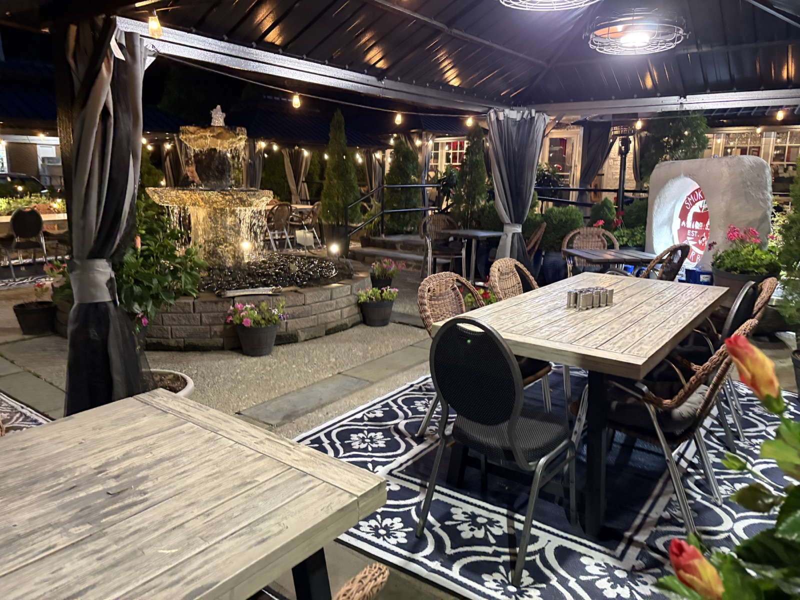 Smoky Rock’s evening patio with a lit fountain, flowers, and covered tables